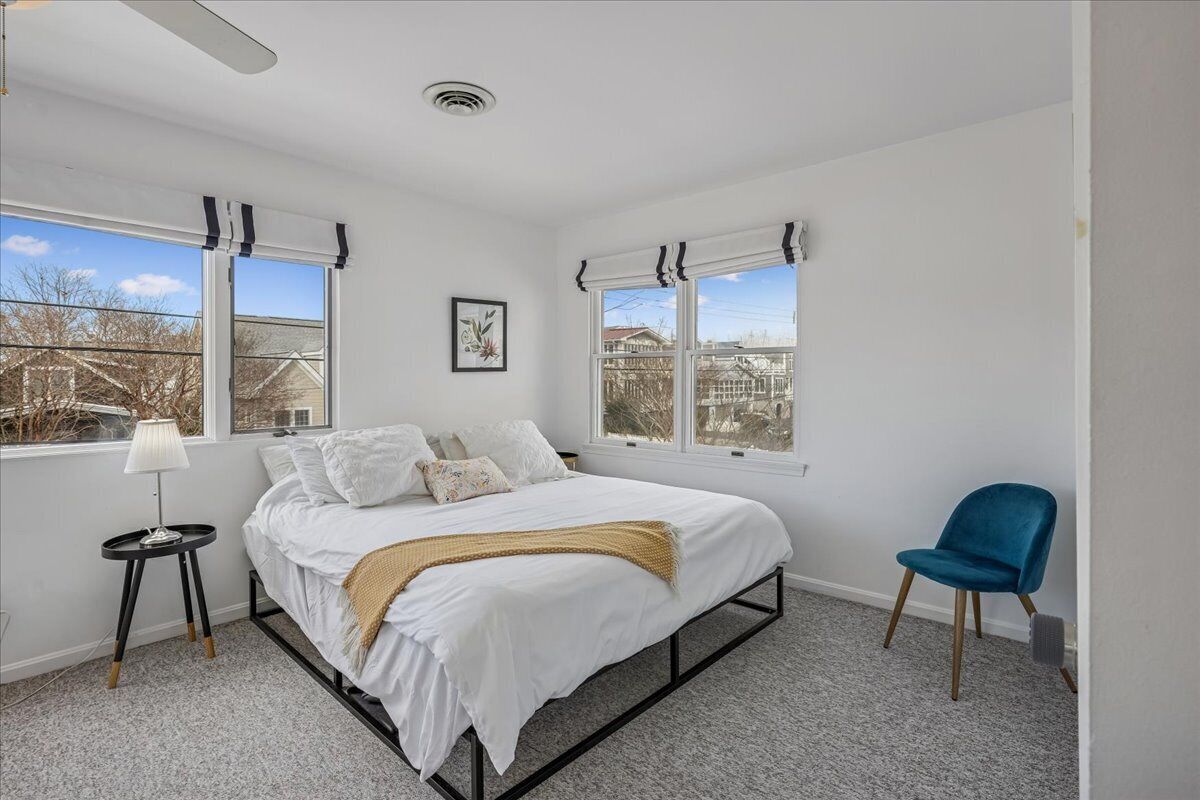 A bedroom with a bed, a chair, a lamp, and two windows with curtains.