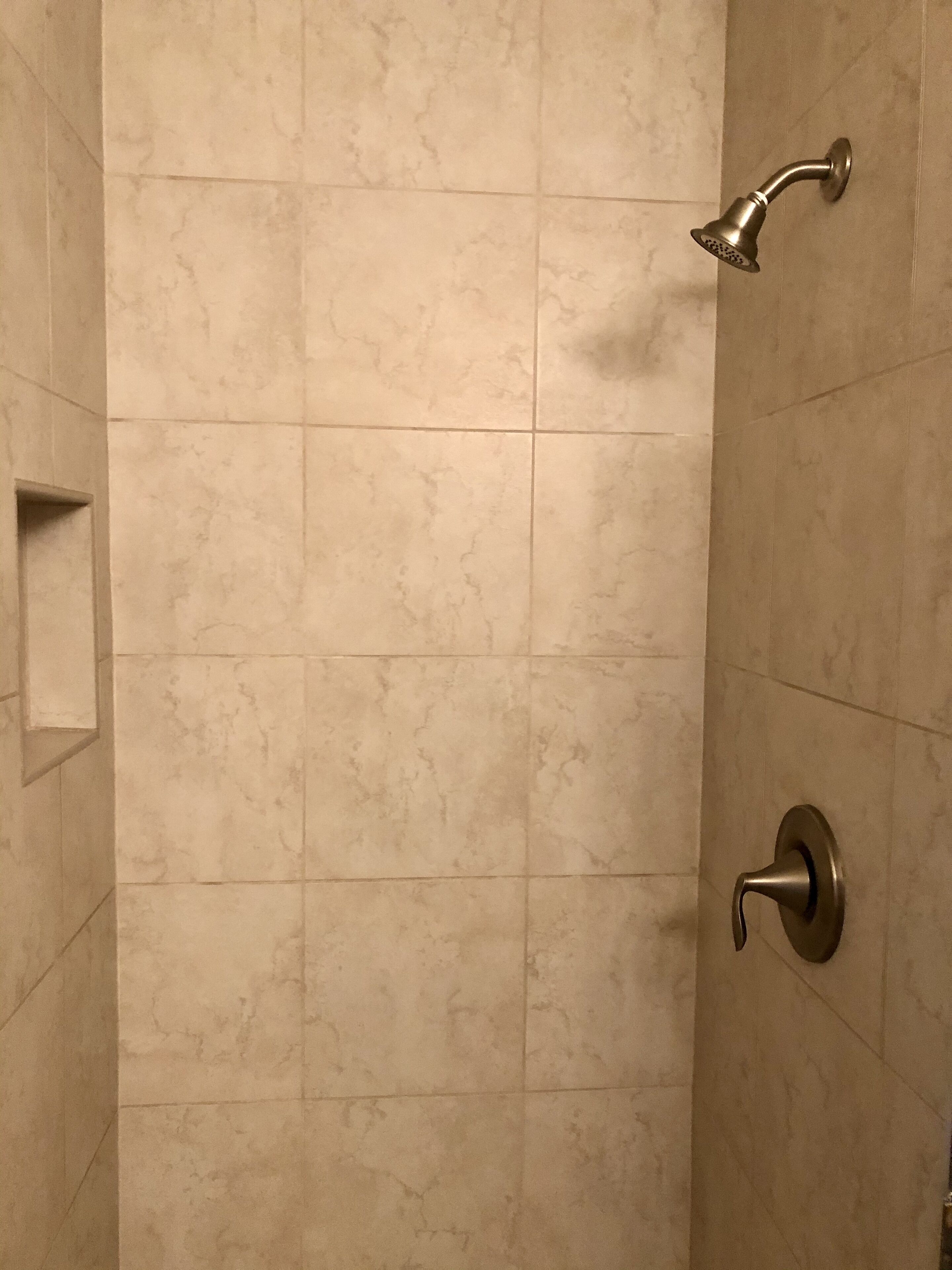 A shower with a handheld showerhead and a wall-mounted faucet in a tiled bathroom.