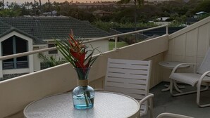 A balcony with a round table and two chairs, overlooking a sunset with palm trees and houses in the background. - POIPU - ENJOY THE VIEWS!   
MANUALOHOA #506  w/NEW SPLIT A/C SYSTEM (Koloa)