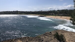 A coastal view with a beach, ocean waves, and a distant resort area. - POIPU - ENJOY THE VIEWS!   
MANUALOHOA #506  w/NEW SPLIT A/C SYSTEM (Koloa)