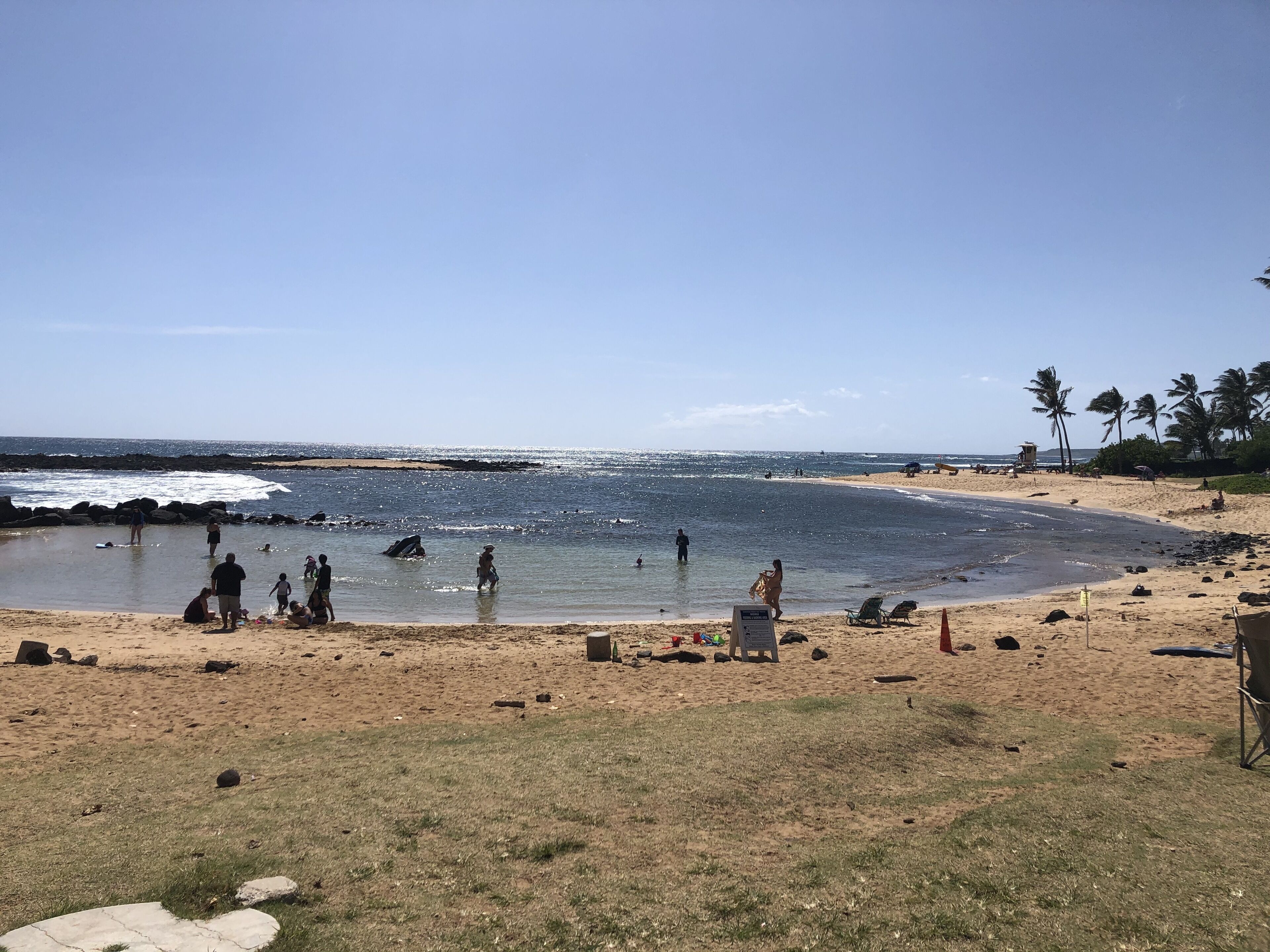 Ein Strand mit Menschen, die das Wasser genießen, einem Rettungsturm und Palmen im Hintergrund.