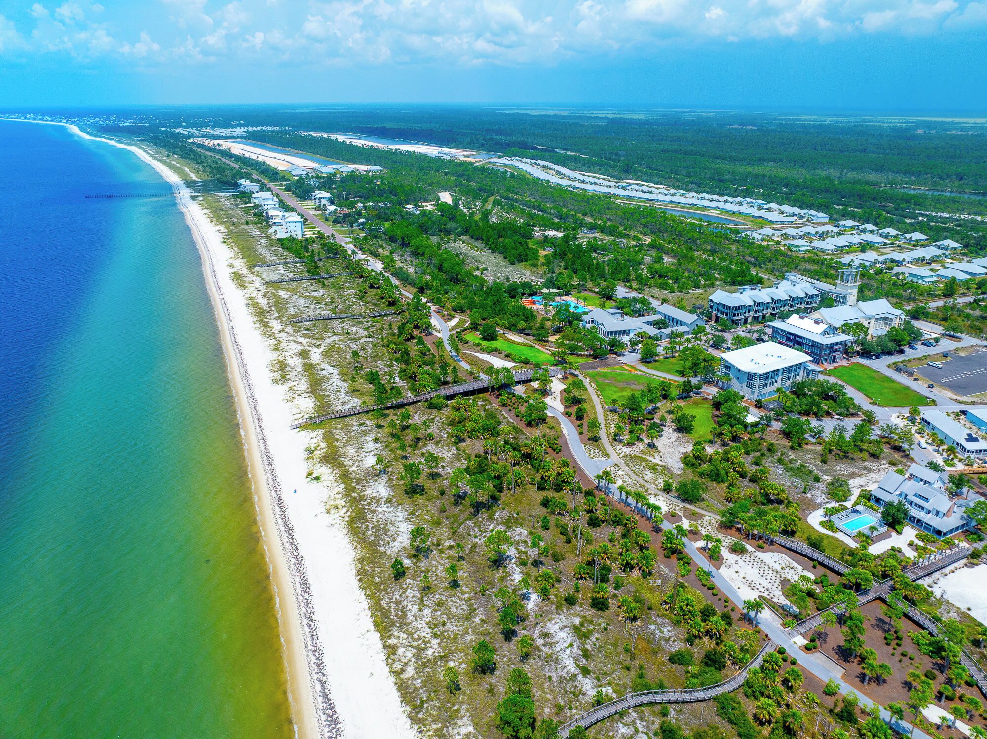 Vista aérea de un complejo turístico costero con propiedades frente al mar, un campo de golf y un amplio estacionamiento.