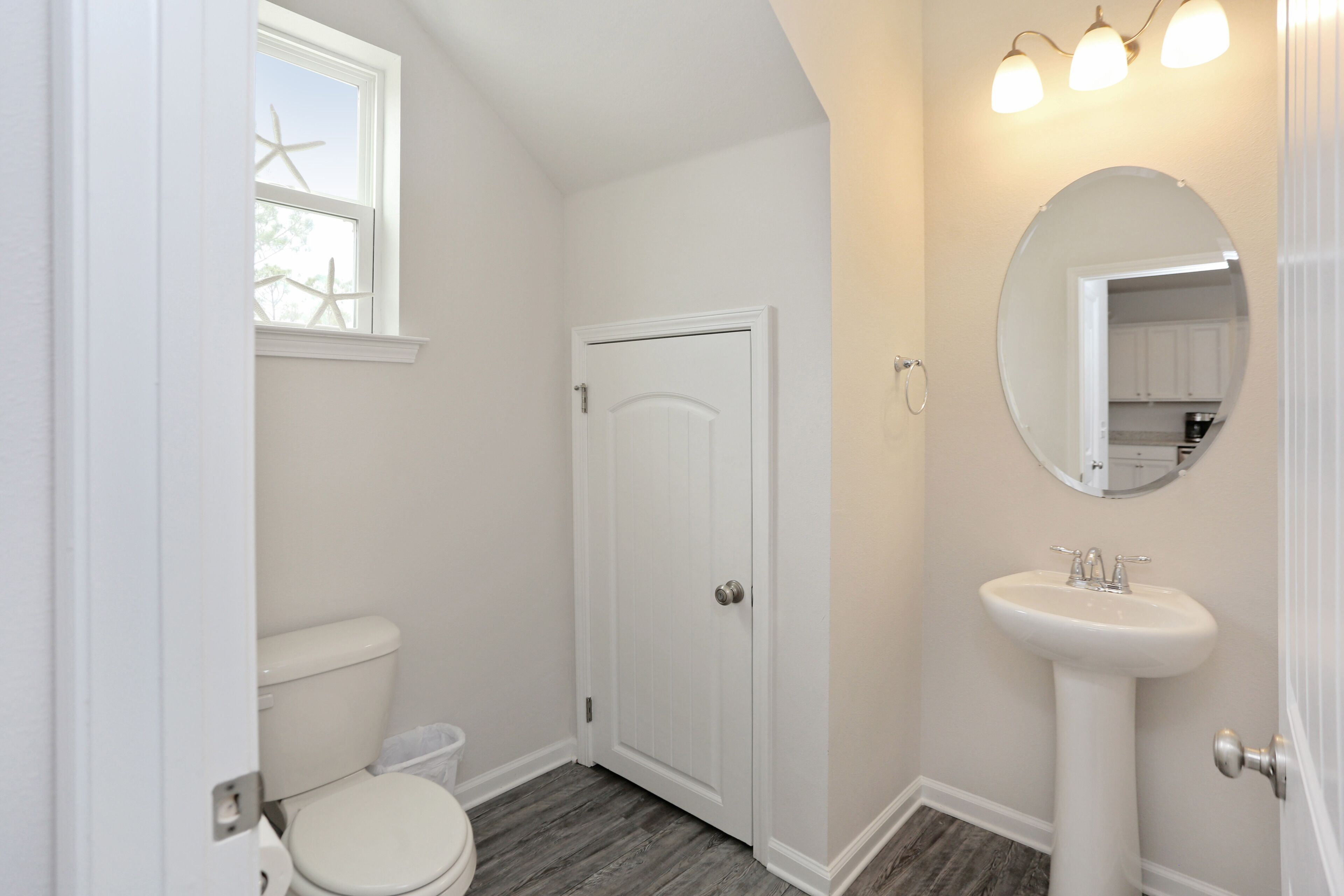 A bathroom with a toilet, a sink, a mirror, and a window with starfish decorations.