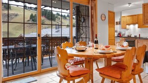 A dining area with a large table, wooden chairs, and a view of a hillside through large windows. - Beautiful apartment for 4 people with WIFI, TV, balcony and pets allowed (Les Crosets)