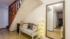 Una escalera con escalones de madera, un banco blanco con mantas dobladas, un espejo y un jarrón decorativo con luces.