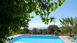 Una piscina rectangular con borde de piedra, rodeada por un muro de piedra y algunos árboles.