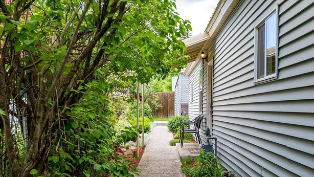 Un étroit sentier mène à une maison dotée d’un porche, entourée d’une végétation luxuriante et d’une clôture en bois.