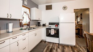 Une cuisine de taille réduite, avec des meubles blancs, une cuisinière, un évier et un réfrigérateur.