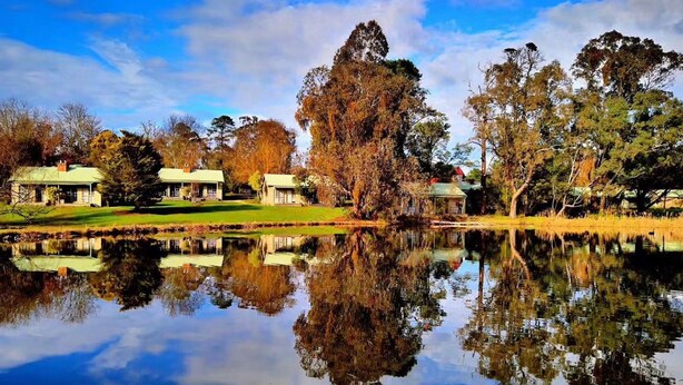 A serene lakeside property with multiple buildings, a clear reflection in the water, and a variety of trees. - Acheron Valley Country Estate (Acheron)