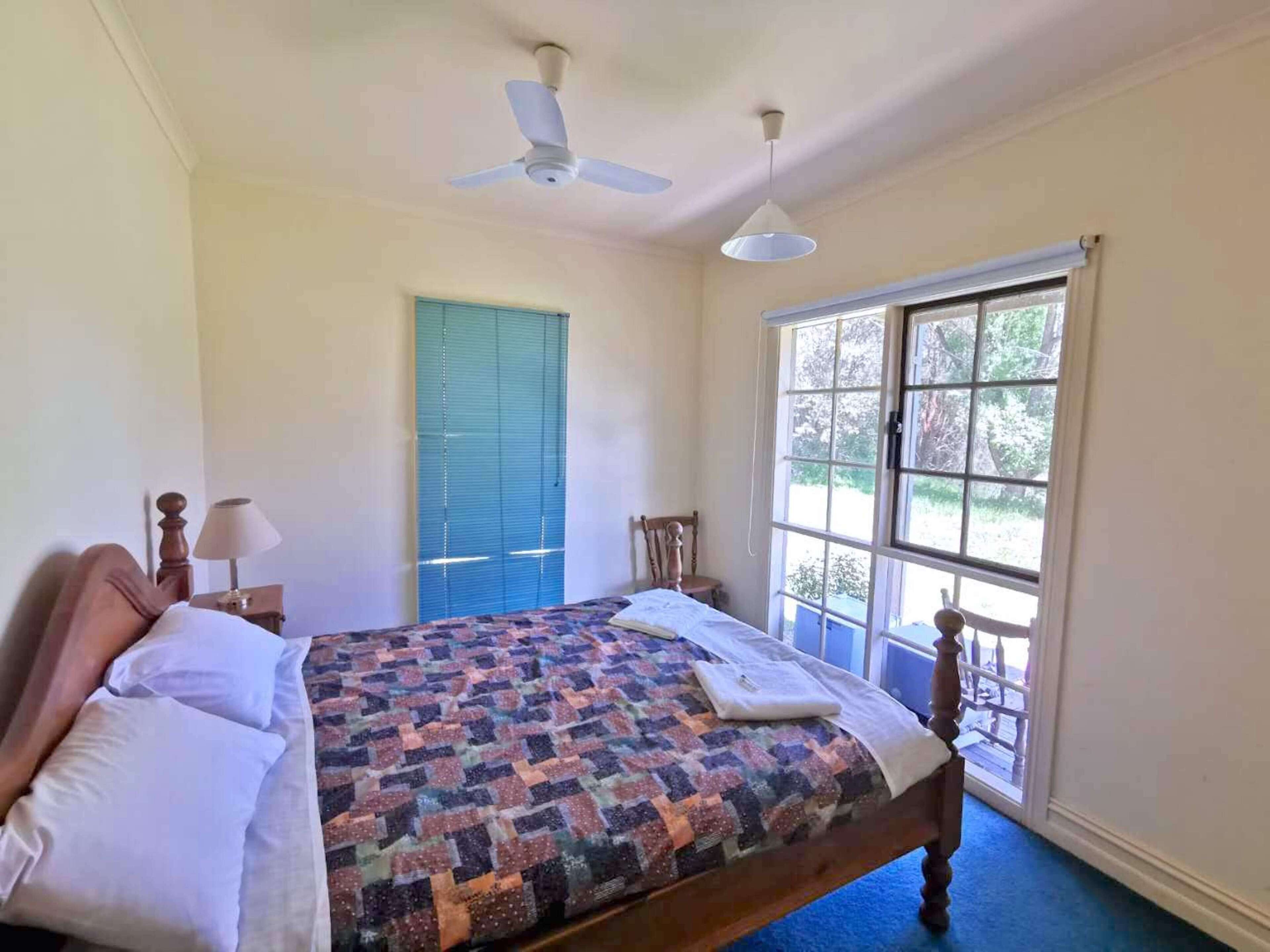 A bedroom with a bed, a ceiling fan, a window with a view, and a blue door.