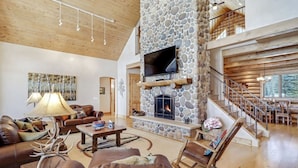 A spacious living room with a stone fireplace, leather furniture, and a wooden staircase. - Home on the 5th Green - Golf, Gameroom, Huge Patio (Angel Fire)