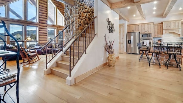 A spacious living area with a wooden staircase, a stone wall, and a kitchen with modern appliances. - Home on the 5th Green - Golf, Gameroom, Huge Patio (Angel Fire)