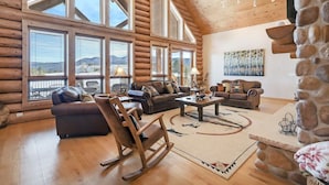 A log cabin interior with a large living area, wooden furniture, and a stone fireplace. - Home on the 5th Green - Golf, Gameroom, Huge Patio (Angel Fire)