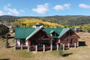 A log cabin with a green roof, stone pillars, and a porch. - Home on the 5th Green - Golf, Gameroom, Huge Patio (Angel Fire)