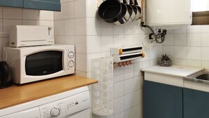 Keittiössä on valkoiset kaapit, mikroaaltouuni, astianpesukone ja kattoteline, johon voi ripustaa kattiloita.
