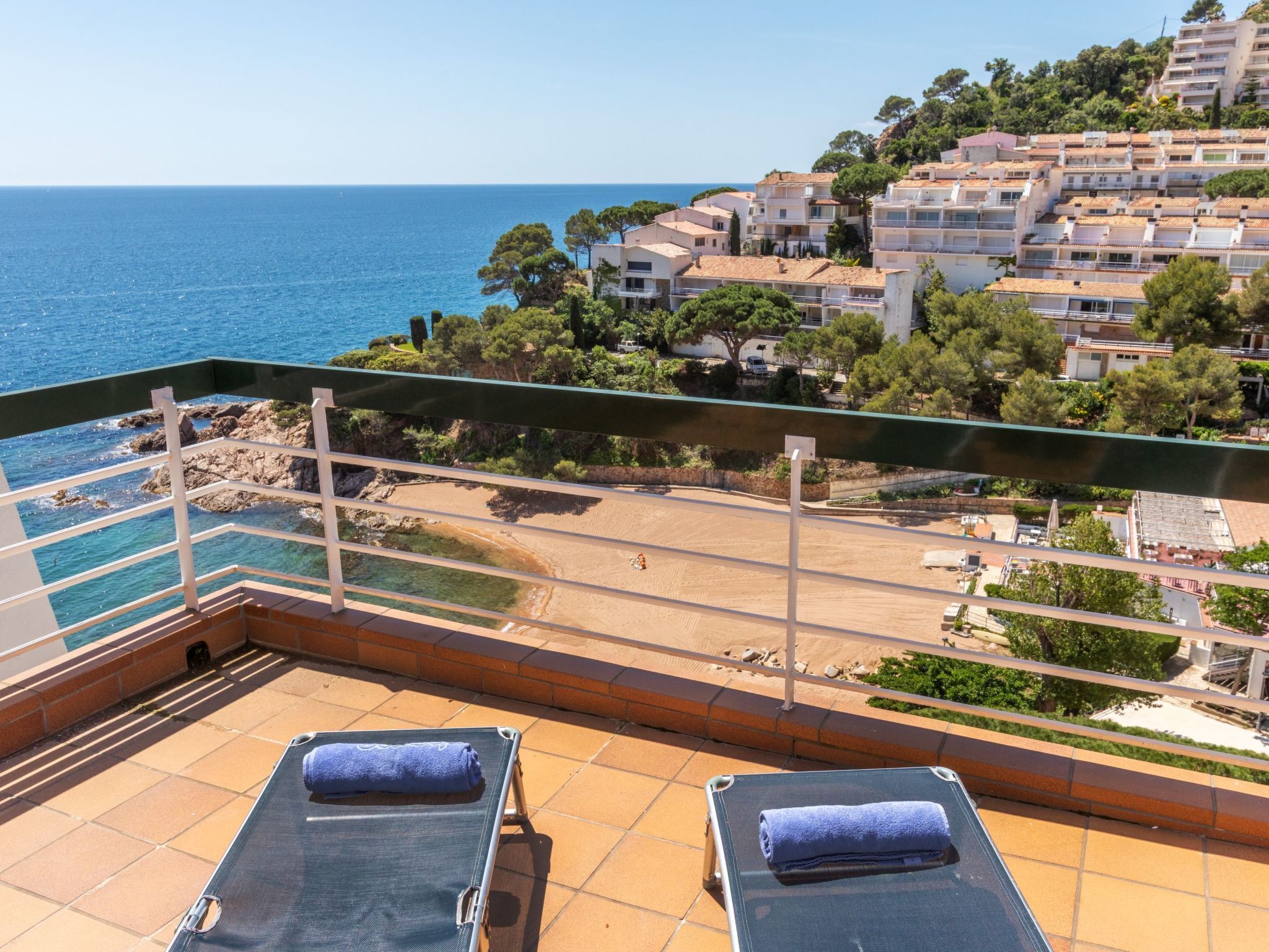 Ein Balkon mit zwei Liegestühlen, freier Blick auf das Meer und eine Küstenstadt im Hintergrund.