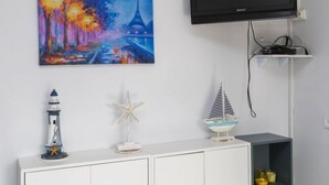Huoneessa on valkoinen kaappi, kuva Pariisin kadusta, televisio ja hylly, jossa on koriste-esineitä.