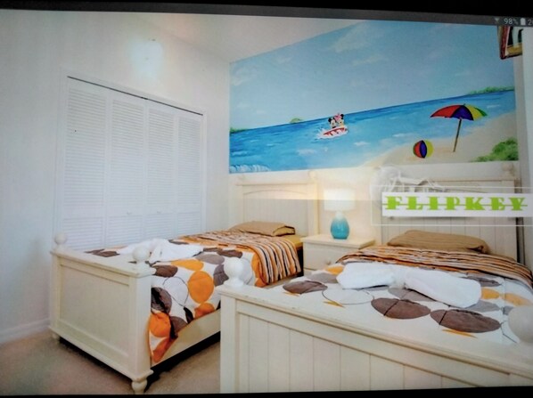 Une chambre avec deux lits, une fresque murale sur le thème de la plage et un panneau indiquant « FLIPKEY ».