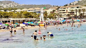 A crowded beach with people swimming and sunbathing, umbrellas, and buildings in the background. - SANDRINE apartment in Benitachell – 2 terraces, swimming pool, air conditioning and Wi-Fi, 1.8 km from Cala Moraig (Benitachell)