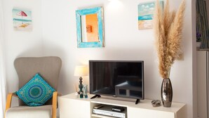 A living room with a television, a chair with a patterned cushion, a vase with pampas grass, and wall art. - SANDRINE apartment in Benitachell – 2 terraces, swimming pool, air conditioning and Wi-Fi, 1.8 km from Cala Moraig (Benitachell)