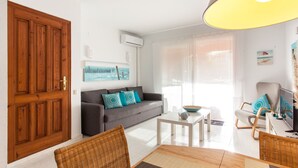 A modern living room with a grey sofa, a white coffee table, wicker chairs, and a large wooden door. - SANDRINE apartment in Benitachell – 2 terraces, swimming pool, air conditioning and Wi-Fi, 1.8 km from Cala Moraig (Benitachell)