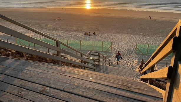 Een houten trap die naar een strand leidt, met een zonsondergang op de achtergrond.