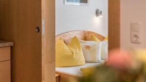 Quarto com cabeceira de madeira, cama com almofadas amarelas e parede branca com interruptor de luz.