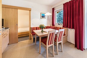 Ein kleiner Raum mit einem Holztisch, einer Bank und einem Fenster mit roten Vorhängen.