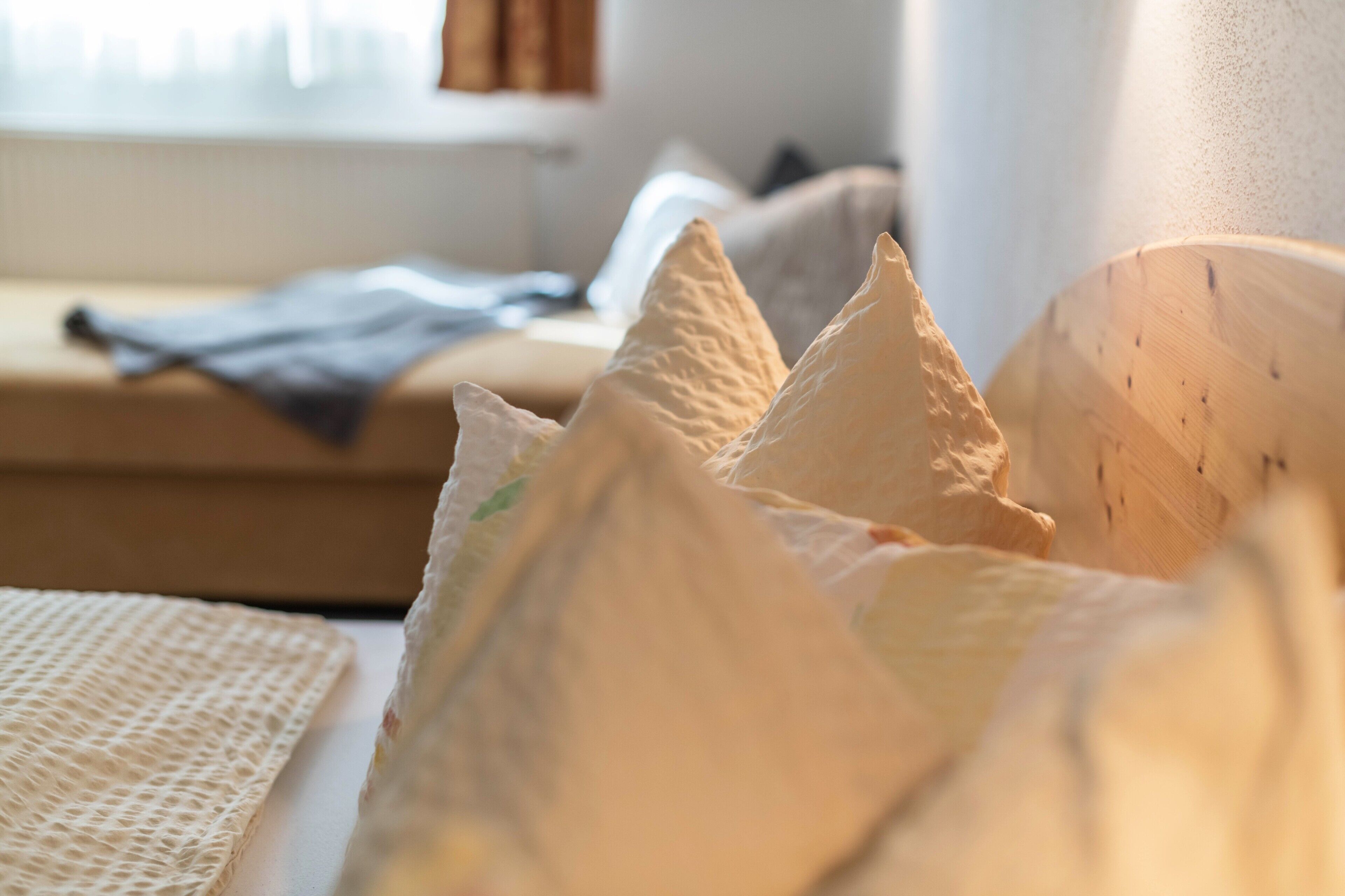 Un lit avec des oreillers et une couverture, une tête de lit en bois et une fenêtre avec des stores.