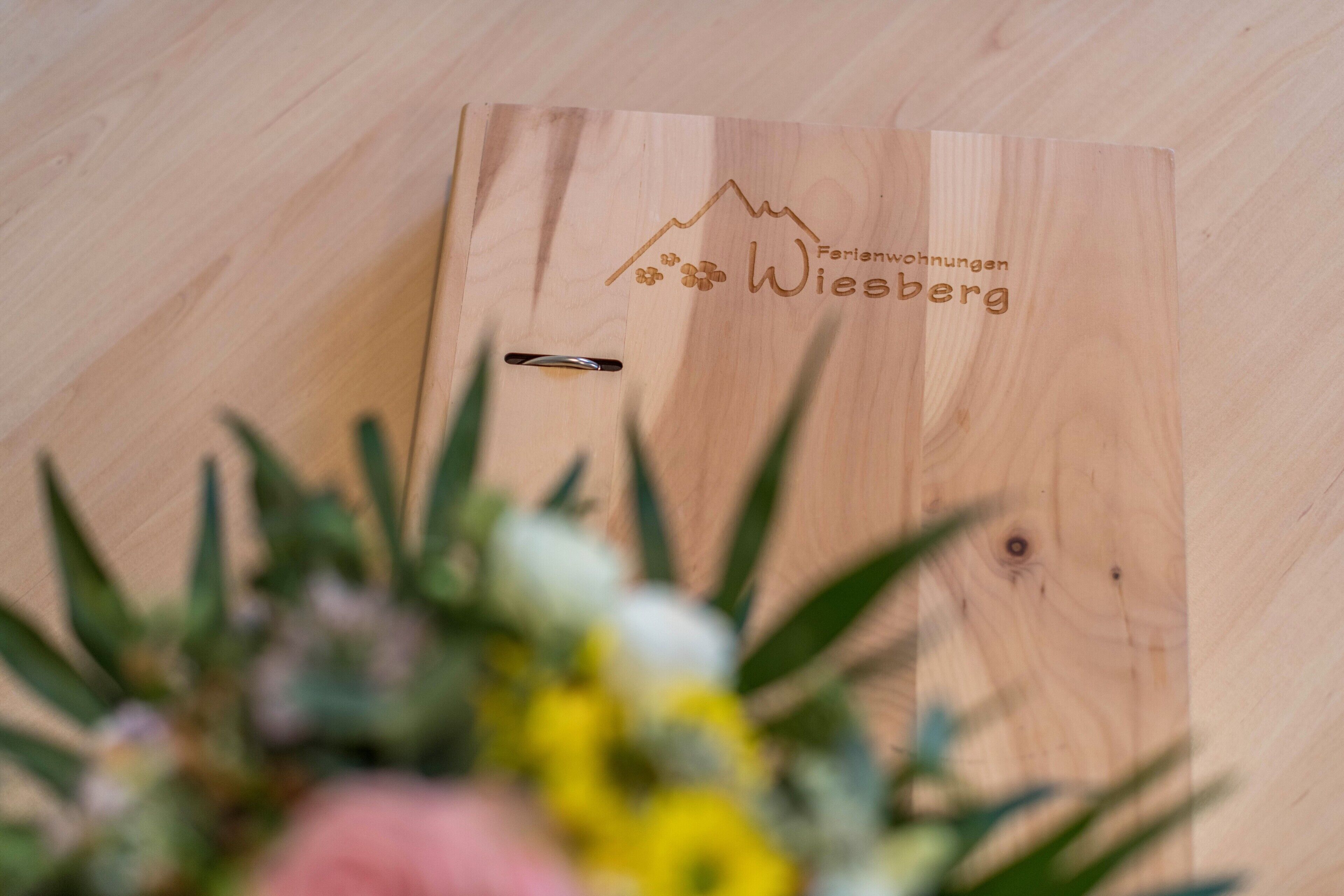 A wooden board with the text 'Ferienwohnungen Wiesberg' and a mountain design.