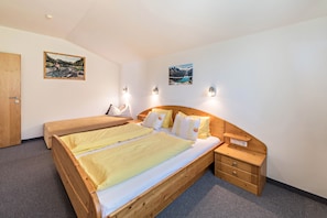 A bedroom with two beds, a wooden headboard, bedside tables, and wall-mounted lights.