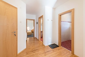 A hallway with wooden flooring, a door with a keyhole, and a tiled shower area.