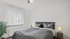 A bedroom with a bed, bedside lamps, a potted plant, and a window with sheer curtains. - Holiday Apartment "Fairschlafen Am See" with Private Terrace & Wi-Fi (Friedrichshafen)