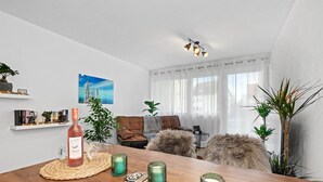 A modern living room with a wooden dining table, green candle holders, a bottle of wine, and a view of the city through large windows. - Holiday Apartment "Fairschlafen Am See" with Private Terrace & Wi-Fi (Friedrichshafen)