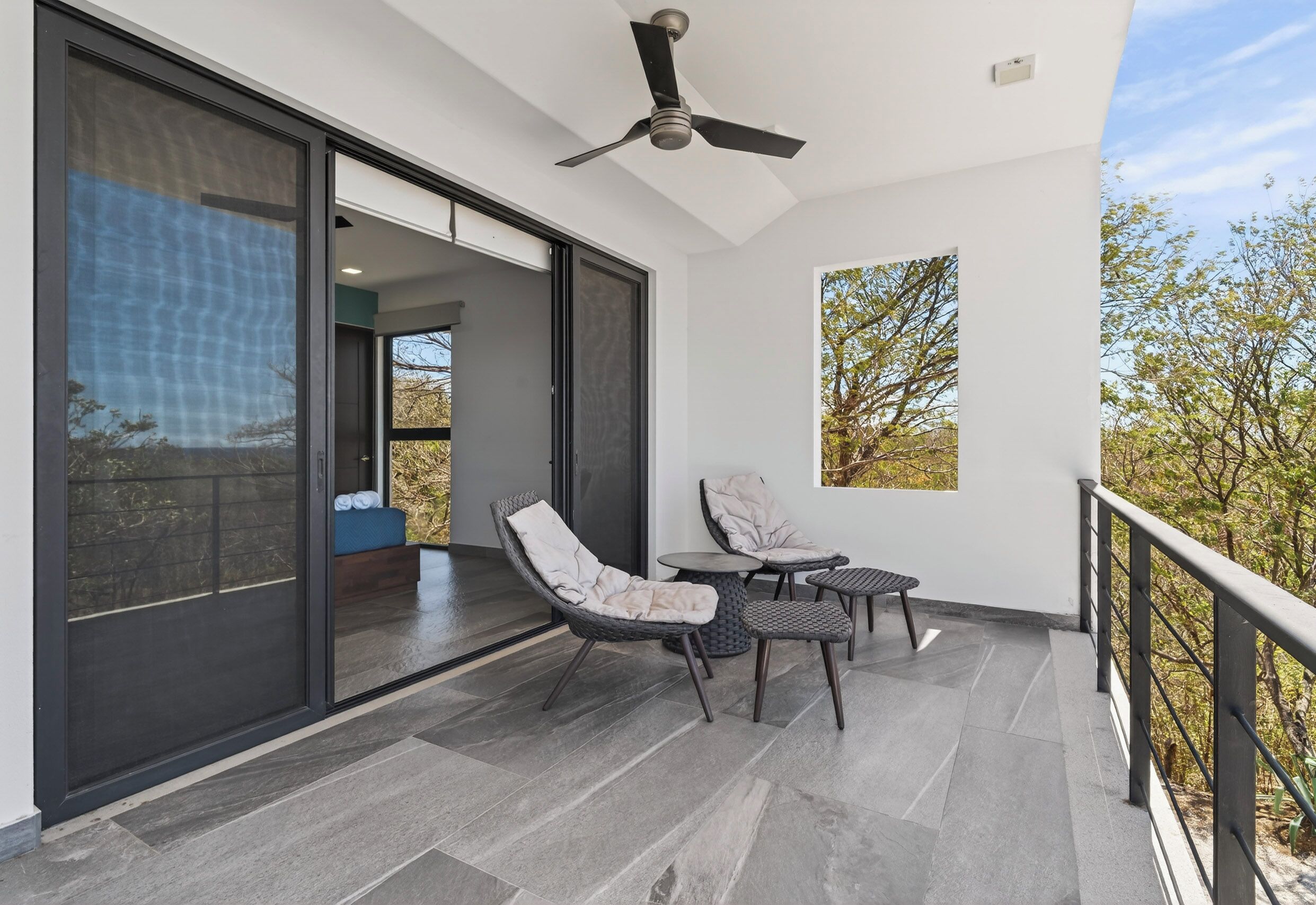 A balcony with a ceiling fan, sliding glass doors, and outdoor seating.