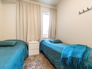 A bedroom with two beds, a nightstand, a lamp, and a window with curtains. - Skivillas 61 ukkohalla (b8) by Interhome (Hyrynsalmi)