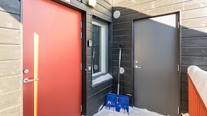 A red door with a window above it, a black door, and a blue snow shovel leaning against the wall. - Skivillas 61 ukkohalla (b8) by Interhome (Hyrynsalmi)