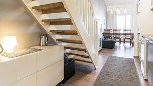 A modern kitchen with a wooden staircase, a dining area with a table and chairs, and a kitchen island with a kettle. - Skivillas 61 ukkohalla (b8) by Interhome (Hyrynsalmi)