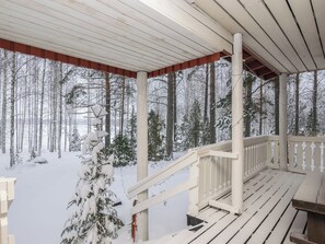 Une véranda en bois avec une balustrade, donnant sur une forêt enneigée.