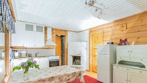 Une cuisine compacte avec des meubles blancs, un îlot central surmonté d’une nappe à motifs floraux, un tapis rouge et un banc en bois.