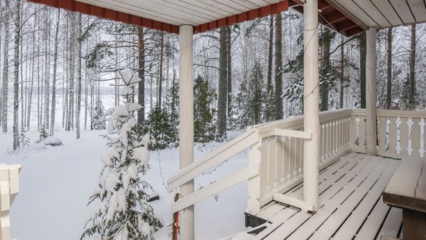 Une terrasse en bois avec une balustrade blanche, entourée d’arbres couverts de neige.