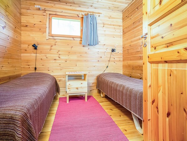 Habitación tipo cabaña con dos camas, una mesita de noche de madera, una ventana con cortinas y una alfombra rosa.
