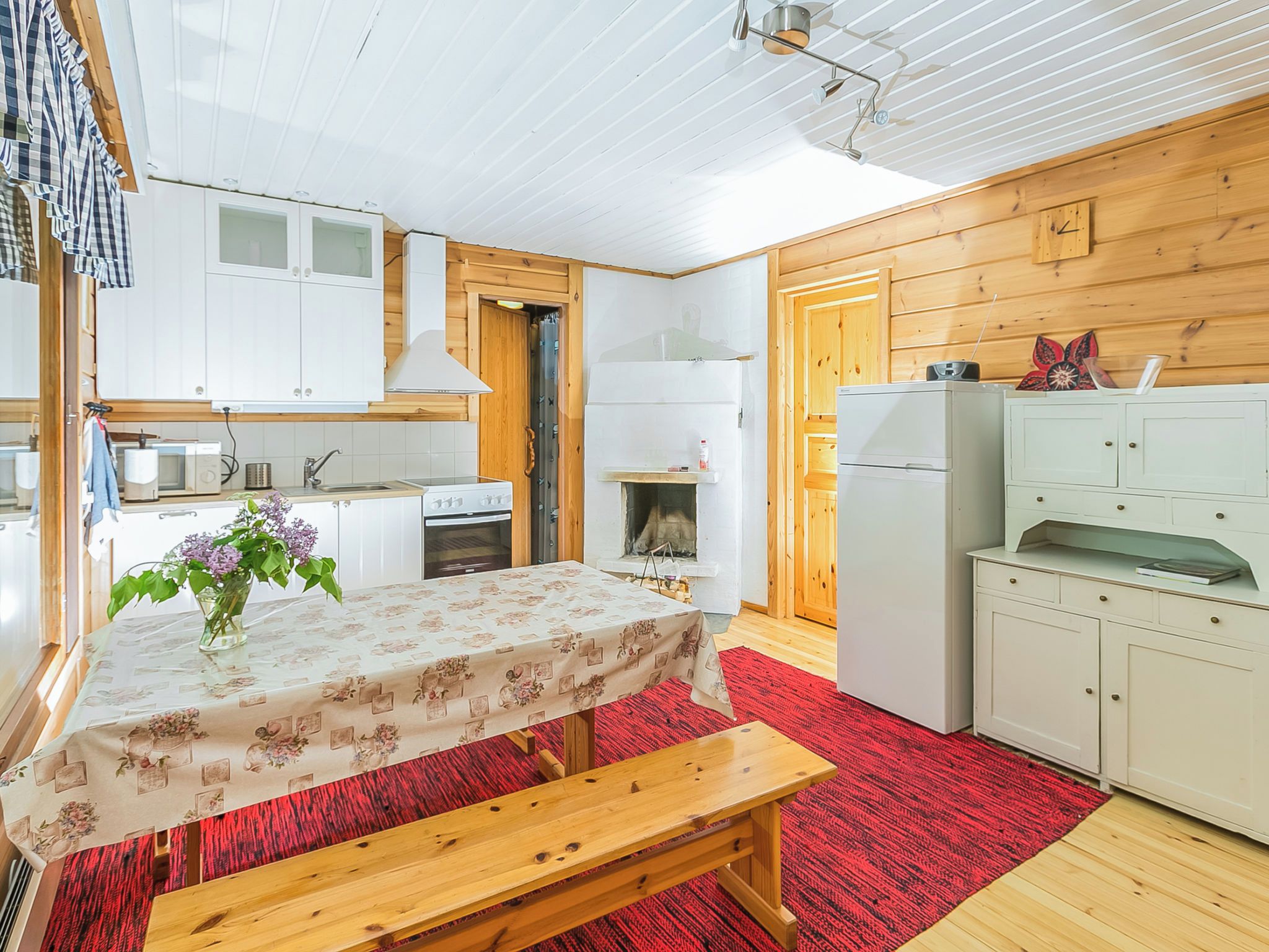 A compact kitchen with white cabinets, a wooden bench, and a red carpet.