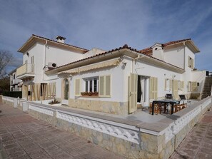 Un bâtiment à deux étages doté d’un balcon, d’un escalier et d’un coin repas aménagé avec du mobilier d’extérieur.