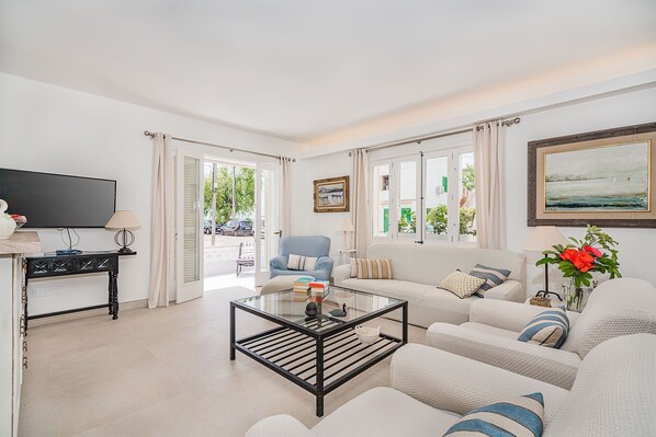 A living room with a glass coffee table, white sofas, a blue armchair, and a TV.