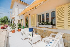 A patio with white wicker furniture, potted plants, and a stone wall.