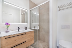 A modern bathroom with a glass shower enclosure, a white sink, and a vanity with wooden drawers.