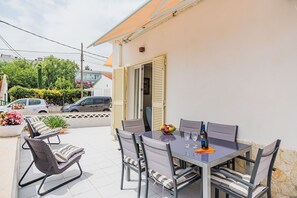 Une terrasse extérieure avec une table et des chaises, une plante en pot et une voiture garée à l’arrière-plan.