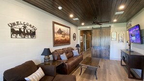 Un vaste salon doté de canapés en cuir, d’un plafond en bois et d’un téléviseur fixé au mur.