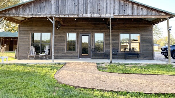 Un bâtiment rustique en bois, doté d’un porche abrité, de grandes fenêtres et d’un espace extérieur aménagé pour s’asseoir.